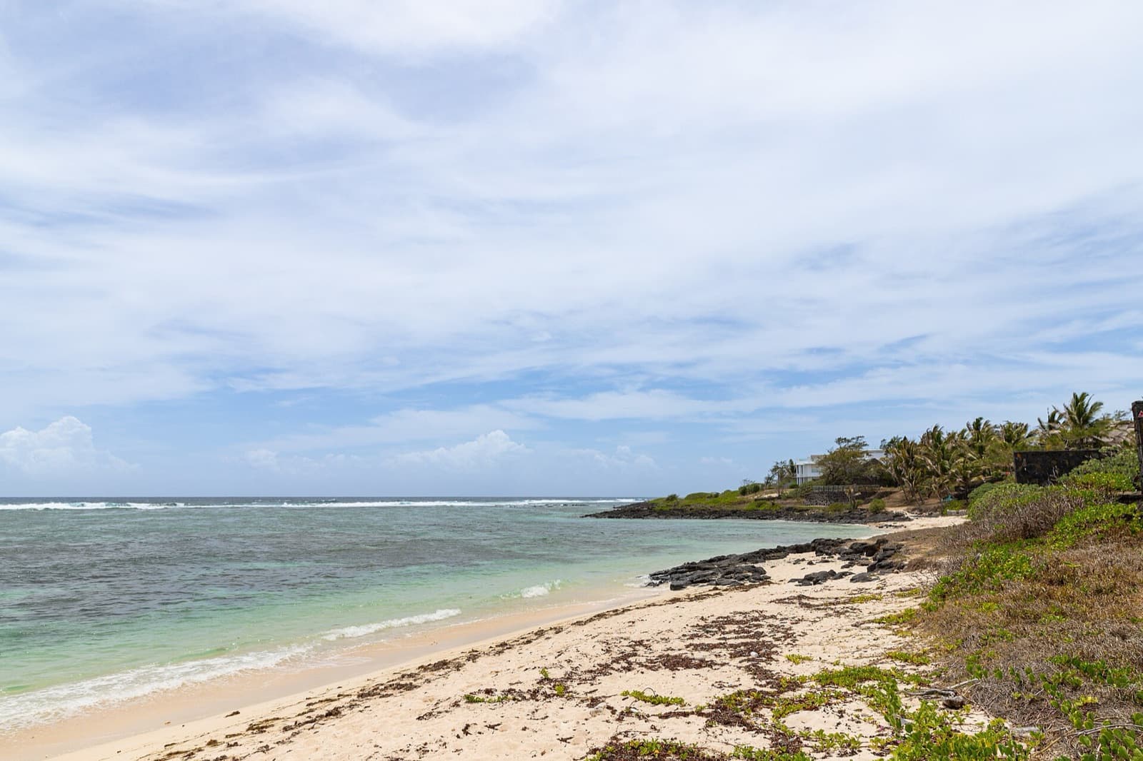 Wit zandstrand met lava-rotsen, turquoise water en palmen aan de oostkust van Mauritius