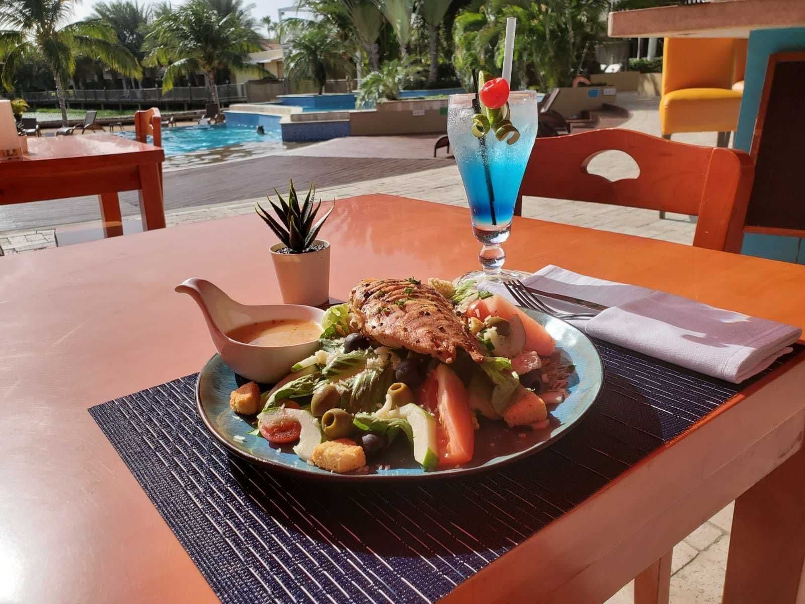 Salade en cocktail op een terrastafel met zwembad op de achtergrond