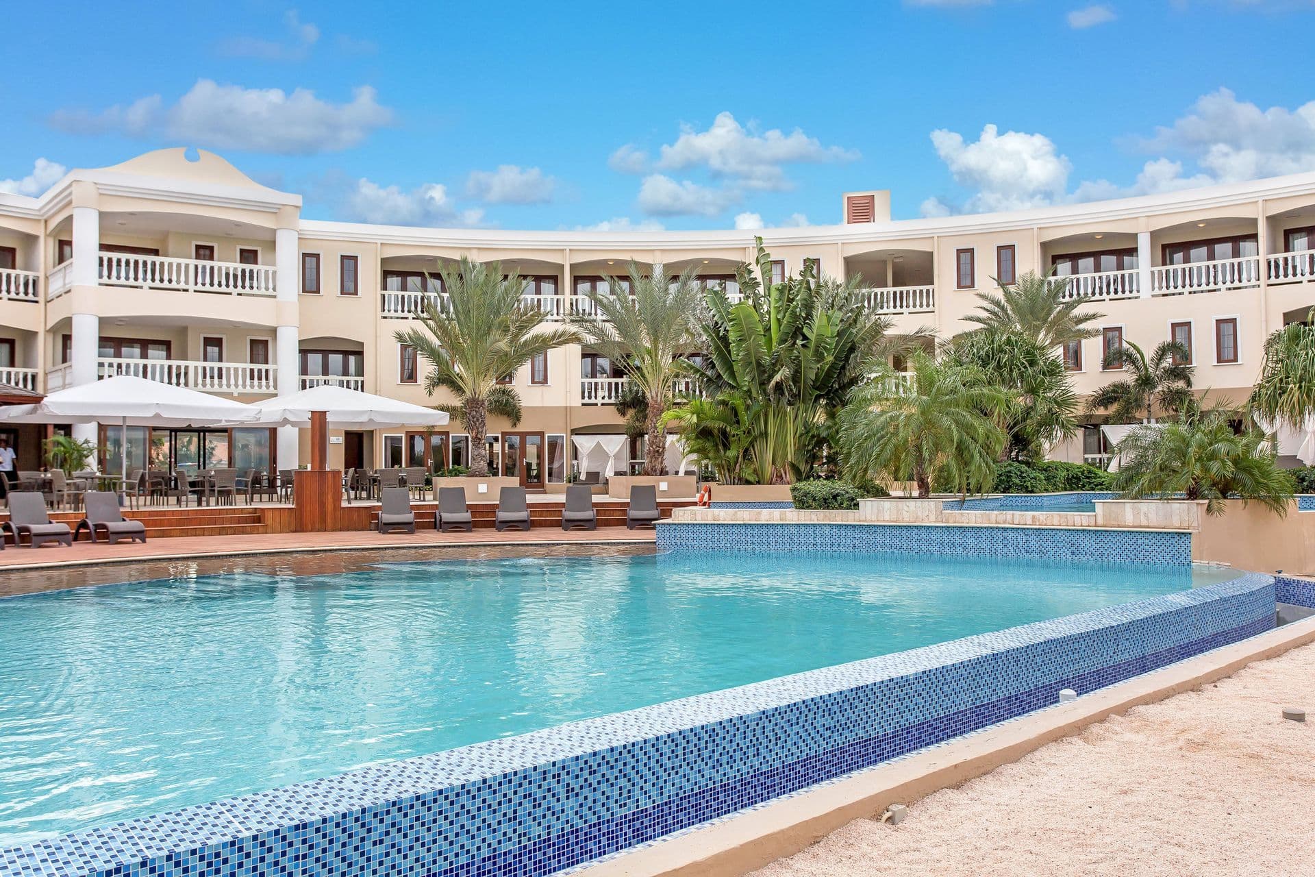 Zwembad en hotelgebouw van ACOYA Curaçao met palmen