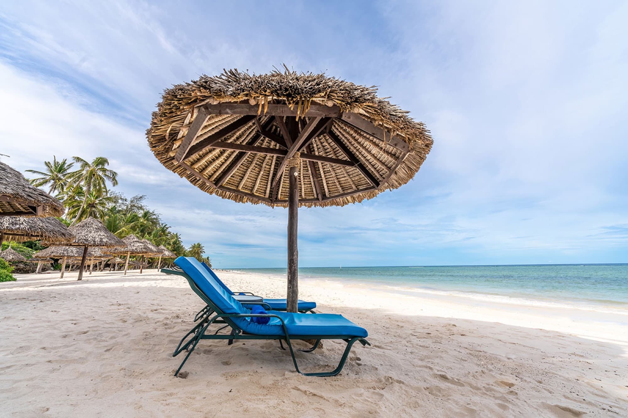 Strand met blauwe ligbedden en parasols van palmblad